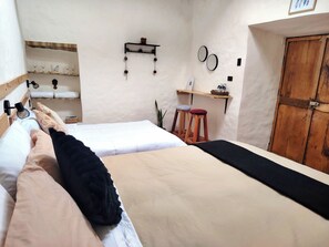 A bedroom with two beds, a wooden door, a shelf with a plant, and a small stool. - KANTIQ House (Cusco)