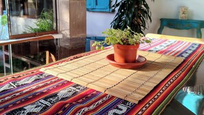 A room with a colorful woven tablecloth, a potted plant, and a blue-framed mirror on the wall.