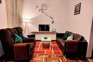 Una sala de estar con dos sofás, una mesa de centro, un televisor, un reloj y un cuadro en la pared.
