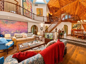 A spacious living area with a high ceiling, a staircase, and a dining area. - The Dome (Big Bear City)