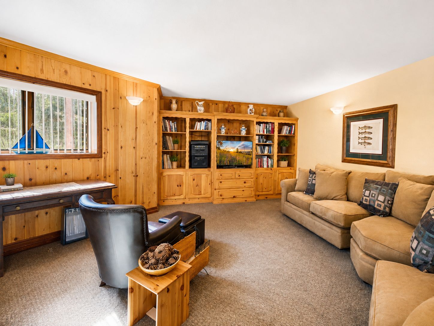 A cozy living room with a wooden bookshelf, a leather sofa, a TV, and a desk with a chair.