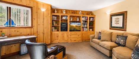 A cozy living room with a wooden bookshelf, a leather sofa, a TV, and a desk with a chair.