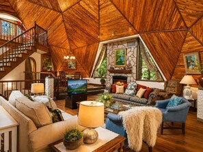 Ein gemütliches Interieur mit Holzbalkendecke, Kamin, einer Couch und einem Fernseher.