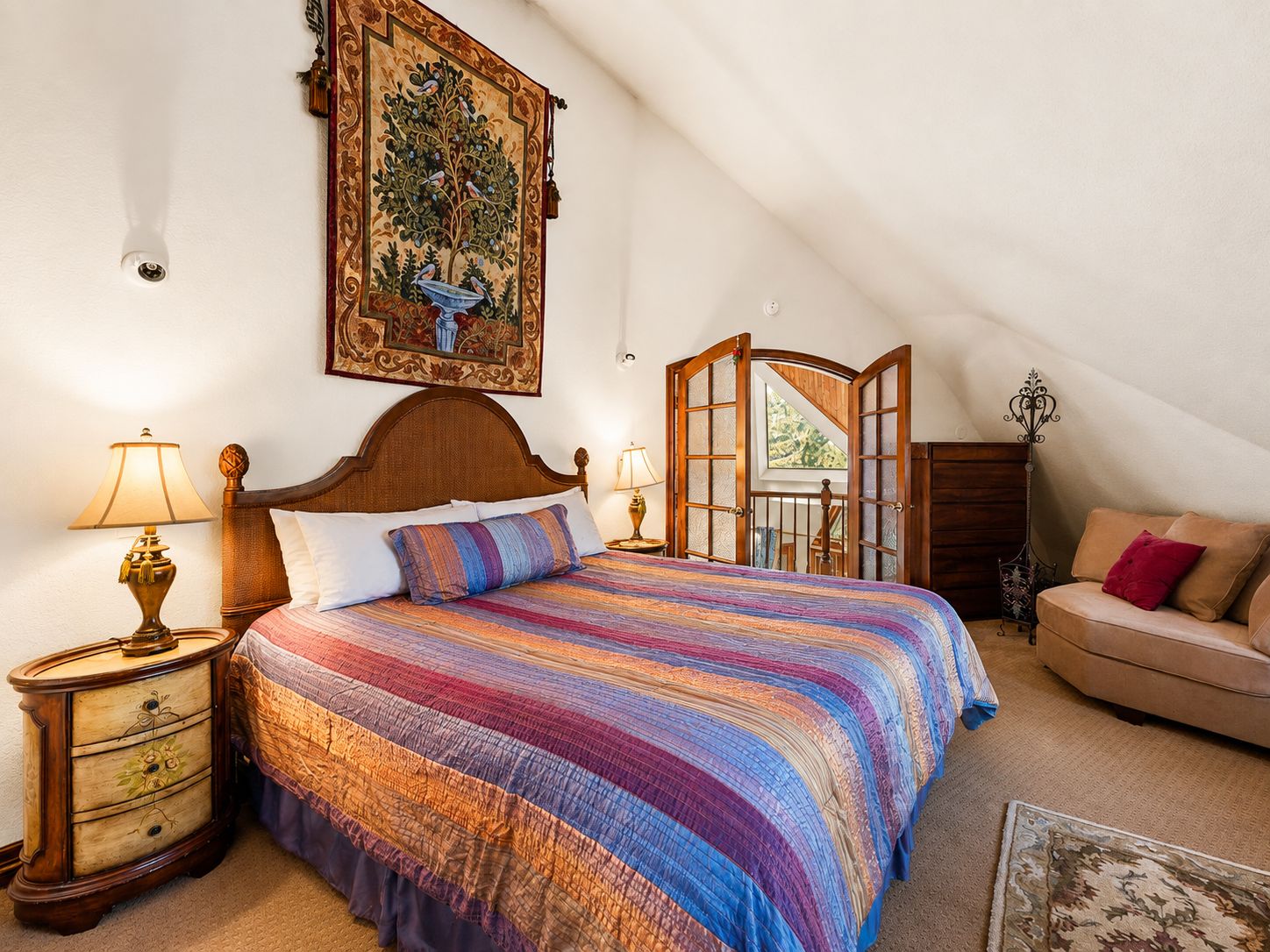 Een slaapkamer met een groot bed, een nachtkastje met een lamp, een dressoir, een sofa en een raam met uitzicht.