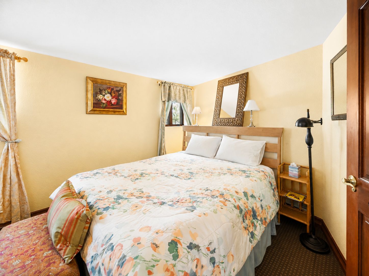 Une chambre d’hôtel avec un lit, une table de chevet, une lampe, un miroir et une fenêtre avec des rideaux.