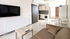 Een knus woongedeelte met een bank, een eettafel, een televisie, een wasmachine en een eethoek.
