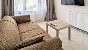 Een moderne woonkamer met een bank, een salontafel en een aan de muur bevestigde televisie.