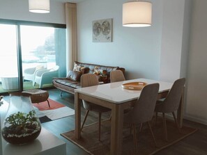 A modern living room with a sofa, dining table, and chairs. There is a large window providing a view of the outdoors. - Vista at Madeira Home Cliff Residence Stunning Sea Views near airport and beach (Gaula)
