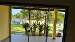 A view through a glass door into a courtyard with potted plants, a tiled floor, and a blue fence in the background. - Spacious house with garden and 3 suites in Novo Airão. (Novo Airão)
