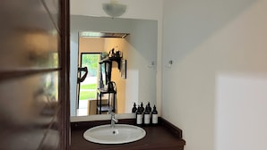 A bathroom with a white sink, dark brown countertop, and a large mirror. There are several bottles of toiletries on the counter. - Spacious house with garden and 3 suites in Novo Airão. (Novo Airão)