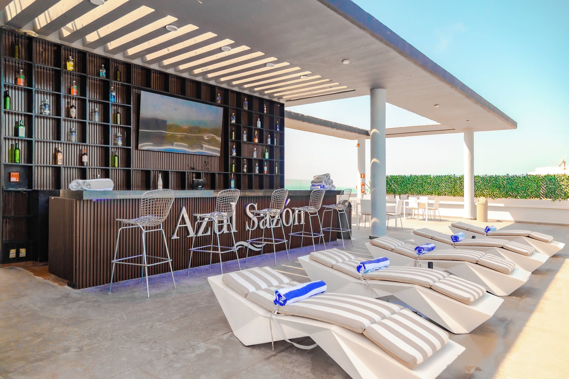 Een terras met een moderne bar, inclusief een toonbank, barstoelen en lounge fauteuils.