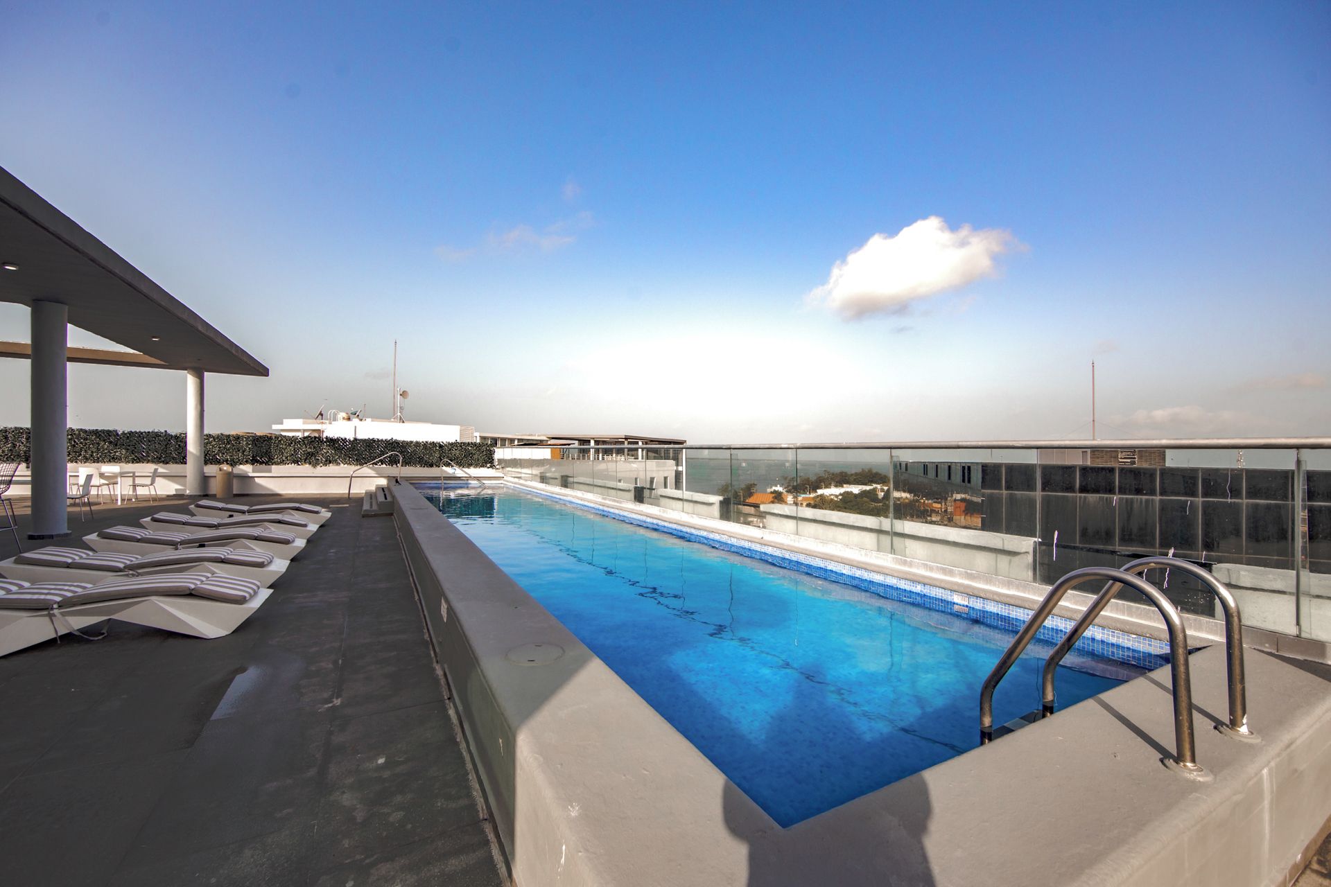 A rooftop swimming pool with lounge chairs and a glass barrier.