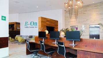 A lobby lounge with a reception desk, three monitors, and a modern chandelier.