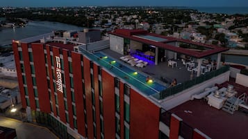 Una terraza de hotel con piscina, sillones de descanso y vistas a la ciudad.