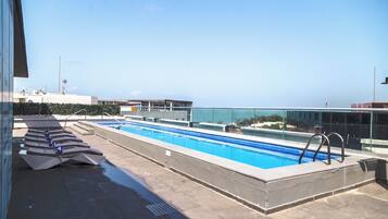 A rooftop swimming pool with a clear view of the sea, a glass barrier, and a set of stairs leading to the pool.