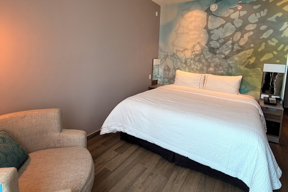 A bedroom with a bed, a chair, a nightstand, and a wall mural.