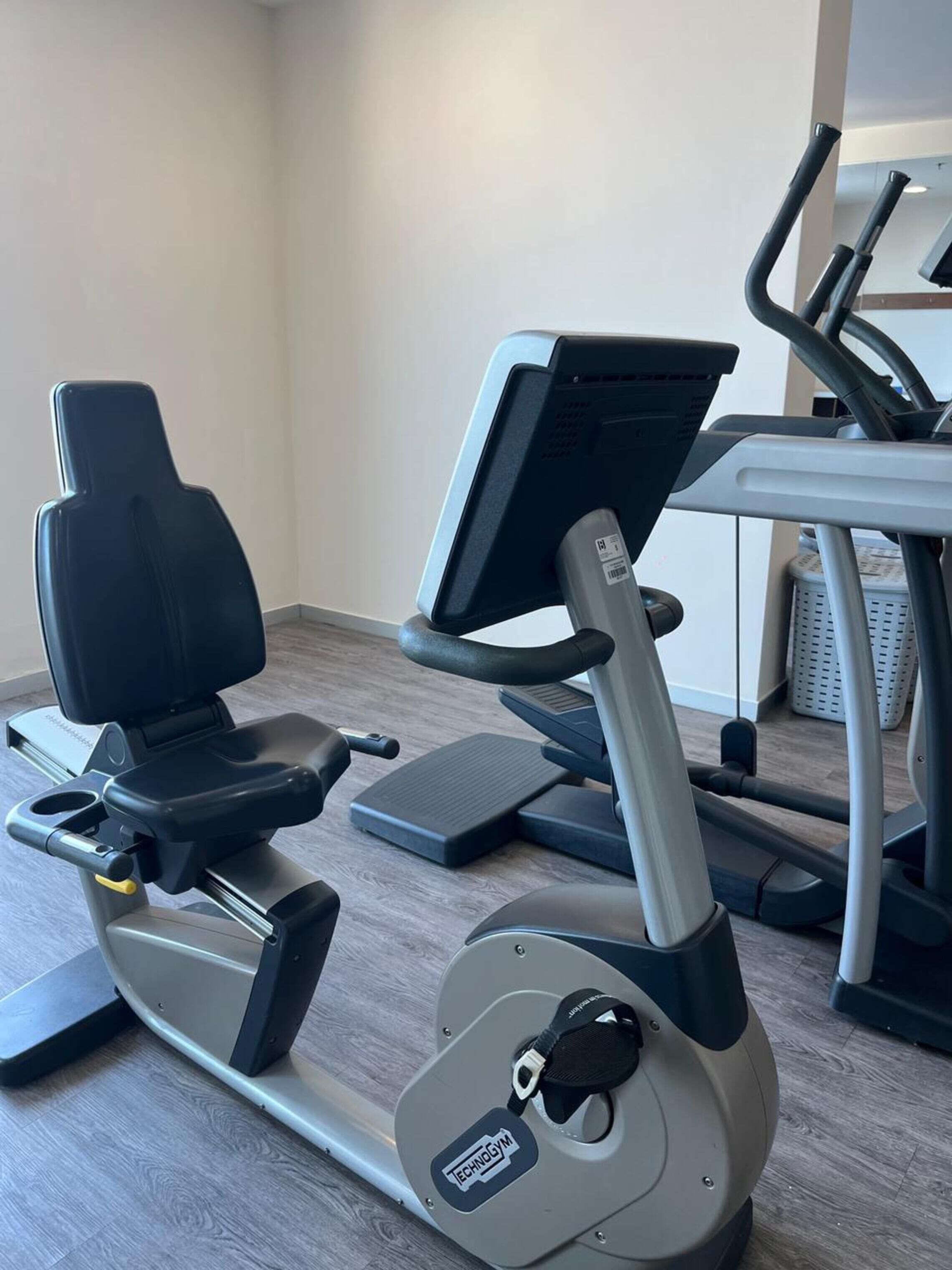 A stationary bike and a treadmill in a room with wooden flooring and a plain wall.