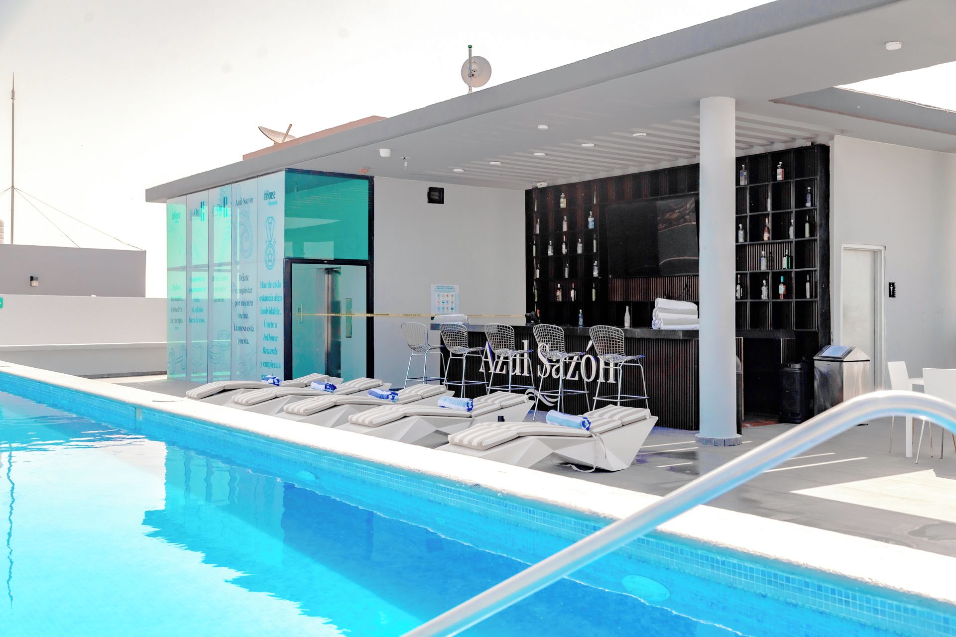 Una piscina con sillones de descanso y una zona de bar con estantes llenos de botellas.