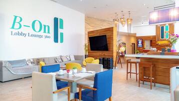 A modern lobby lounge with a sofa, chairs, a table, a TV, and a bar area.