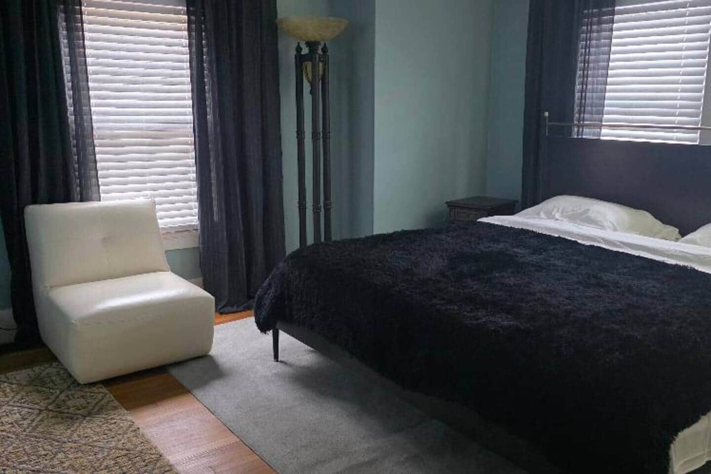 Een slaapkamer met een bed, een stoel, een vloerlamp en een nachtkastje.