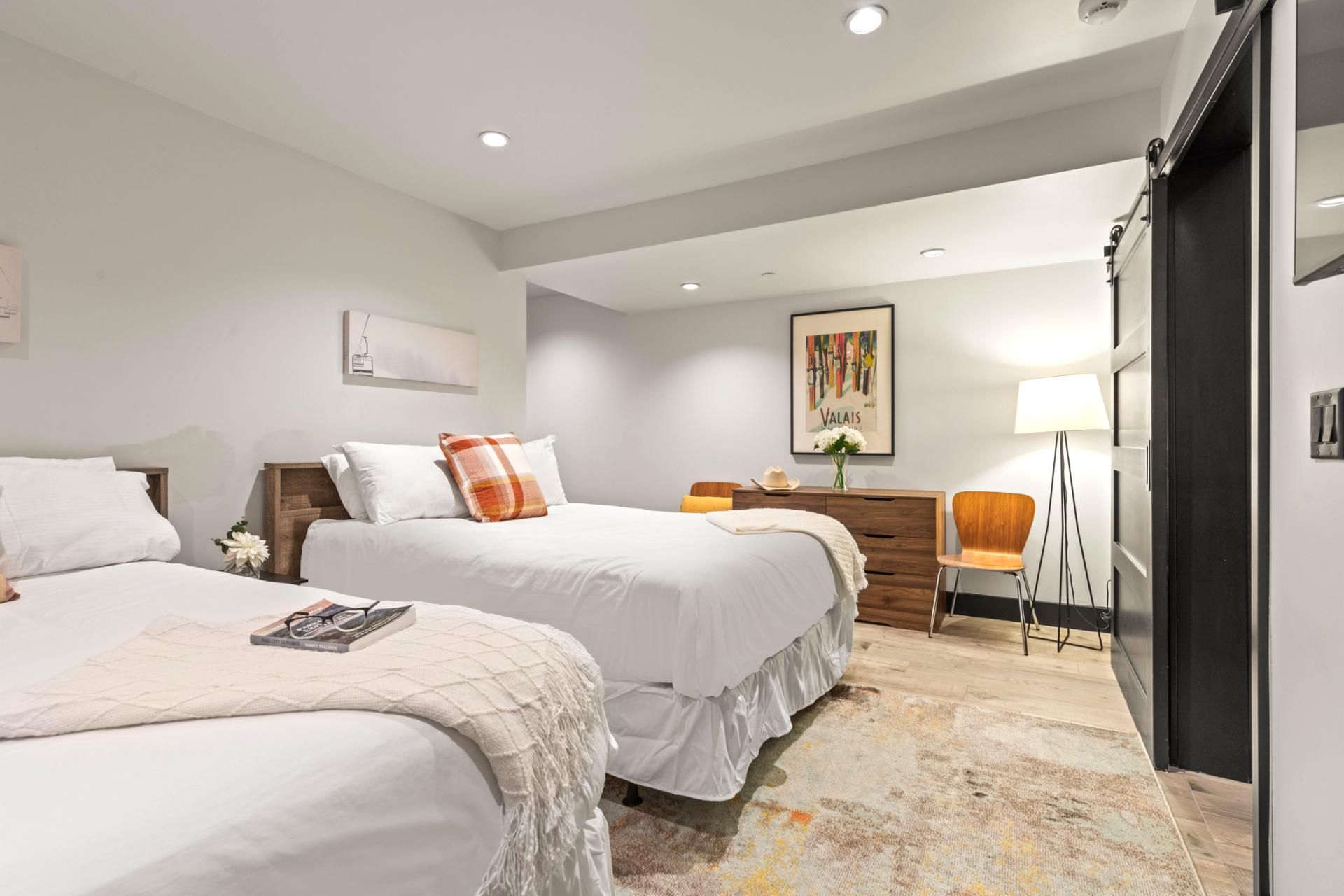 Une chambre d’hôtel avec deux lits, un bureau, une chaise, une lampe et un tableau au mur.