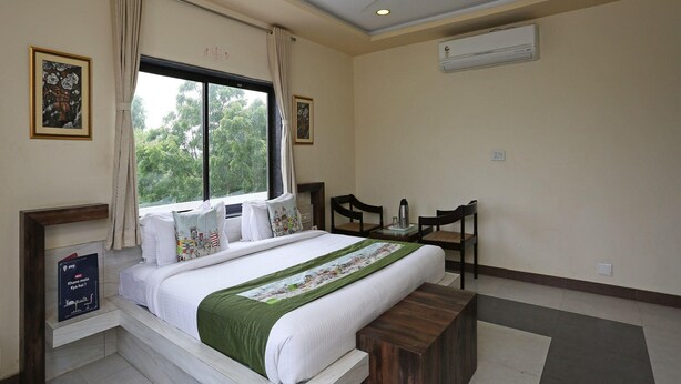 A bedroom with a bed, a desk, chairs, a window with curtains, and an air conditioning unit. - Townhouse Reti Bus Terminal Udaipur (Udaipur)