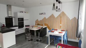 Een moderne keuken met witte kasten, een eethoek met een witte tafel en blauwe stoelen, en een kleurrijk gestreept kussen op de vloer.