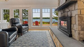 Ein gemütliches Wohnzimmer mit Kamin, Ledersesseln und Seeblick durch große Fenster.