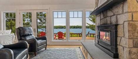A cozy living room with a fireplace, leather chairs, and a view of a lake through large windows.