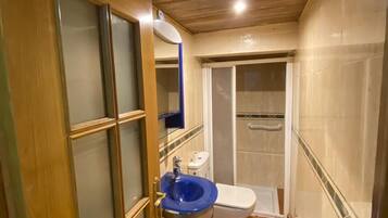 Un baño estrecho con puerta de madera, un lavabo azul, un inodoro y una zona de ducha.