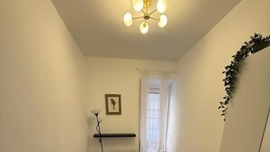 Quarto com cama, mesa de cabeceira, luminária, radiador e janela com cortinas.