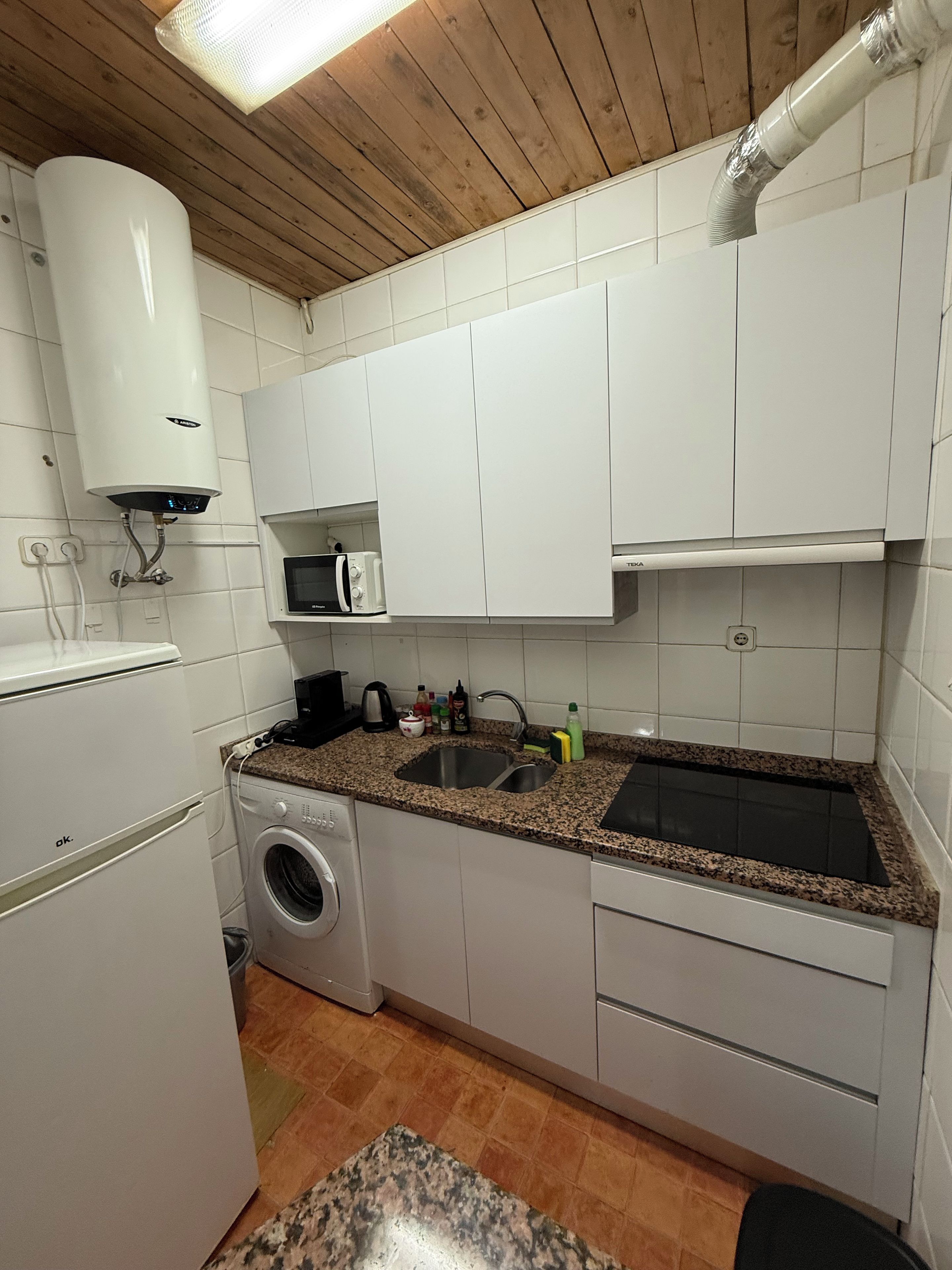A compact kitchen with white cabinets, a built-in washing machine, a microwave, and a sink.