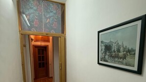 Un couloir étroit au plancher en bois, une porte au fond et un tableau encadré au mur.