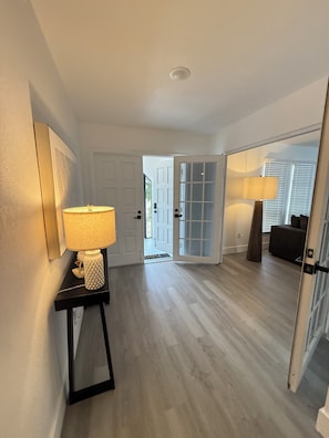 A hallway with a wooden floor, a door leading to an outdoor area, and a lamp on a side table. - Sunny Pool Getaway • Private Yard • Perfect Stay (Cape Coral)