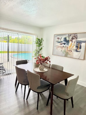 A dining area with a table and chairs, a vase with flowers, and a painting on the wall. - Sunny Pool Getaway • Private Yard • Perfect Stay (Cape Coral)