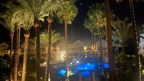 Vista noturna de um resort com palmeiras, piscina e edifícios iluminados.