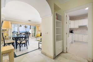 A dining area with a table and chairs, a kitchen with white cabinets, and a view of palm trees through the window. - Sea View at White Pearl Beach II, Elviria, Marbella (Marbella)