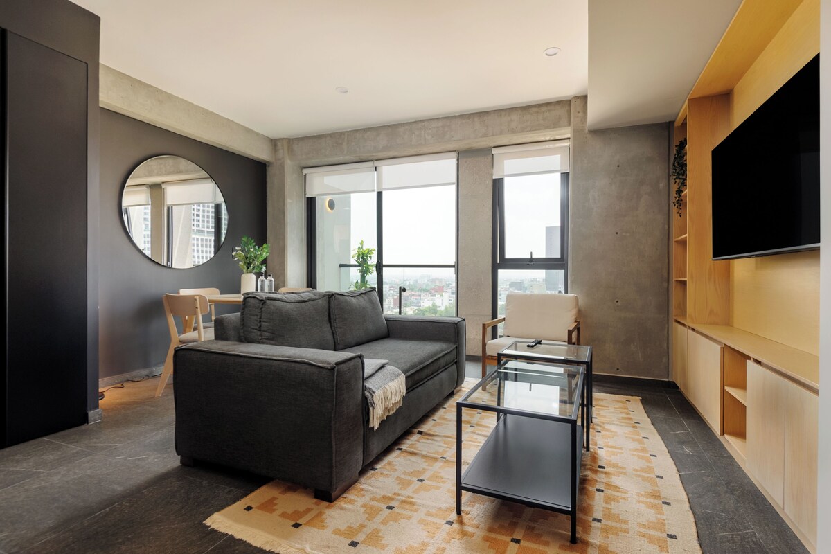 A modern living room with a sofa, a coffee table, a TV, and large windows.
