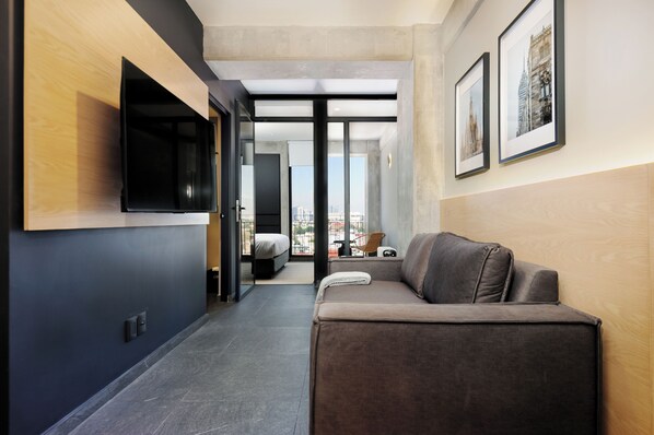 Ein modernes Hotelzimmer mit einer Couch, einem Flachbildfernseher, einem Bett und einem großen Fenster mit Blick auf die Stadt.