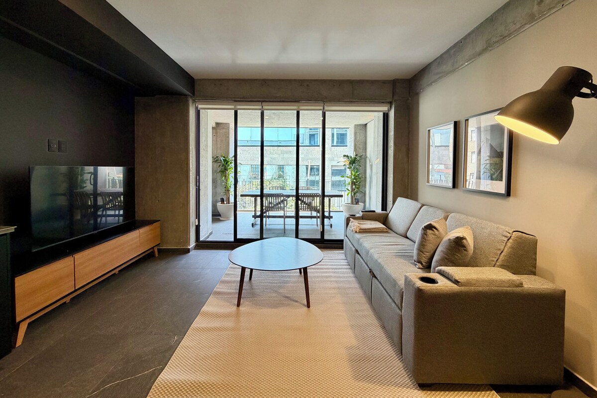 A modern living room with a sofa, a coffee table, a TV, and a large window.