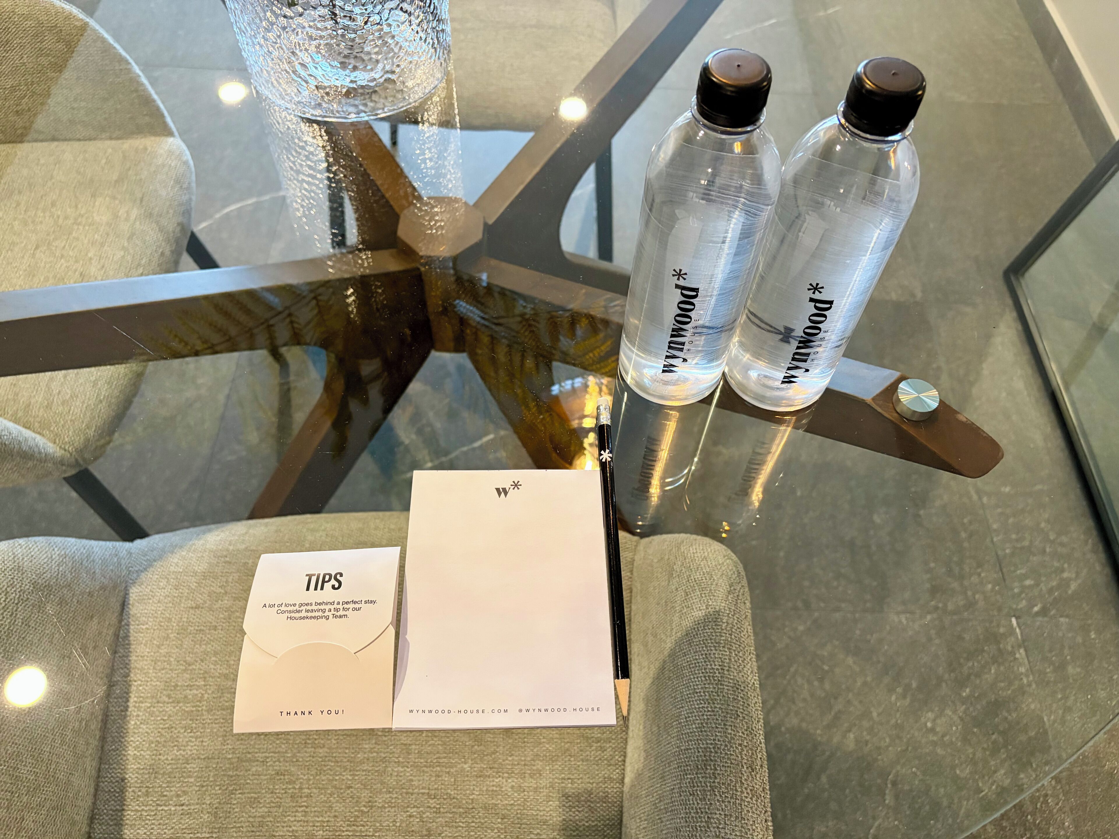 Een glazen tafel met twee waterflessen, een witte envelop met de tekst 'TIPS' en 'BEDANKT!', en een webadres.