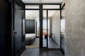 Une chambre d’hôtel moderne, équipée d’un lit, d’une petite table et d’une chaise. Elle dispose également d’un balcon avec vue sur la ville.
