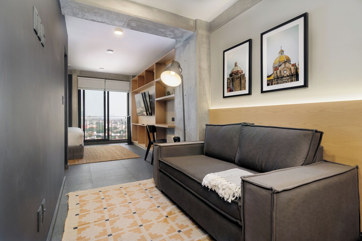 A modern living room with a sofa, a coffee table, and a large window offering a city view.