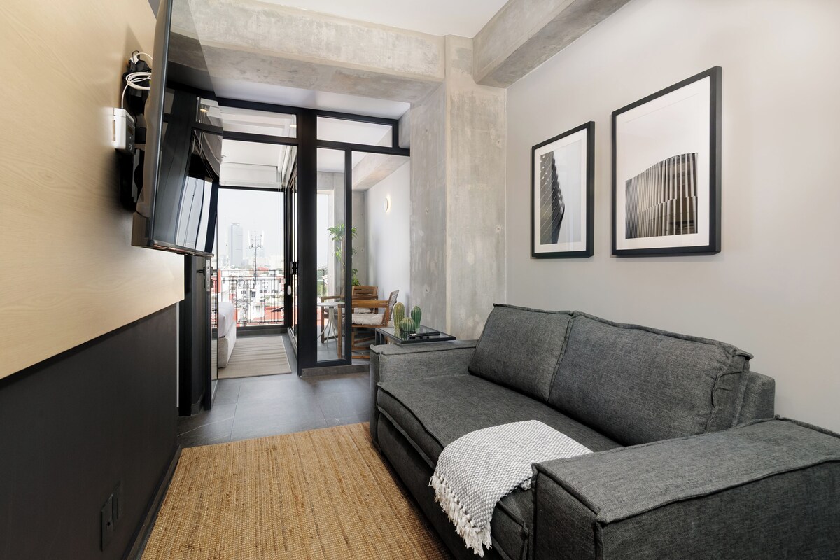 A modern living room with a grey sofa, a flat-screen TV mounted on the wall, and two framed artworks.