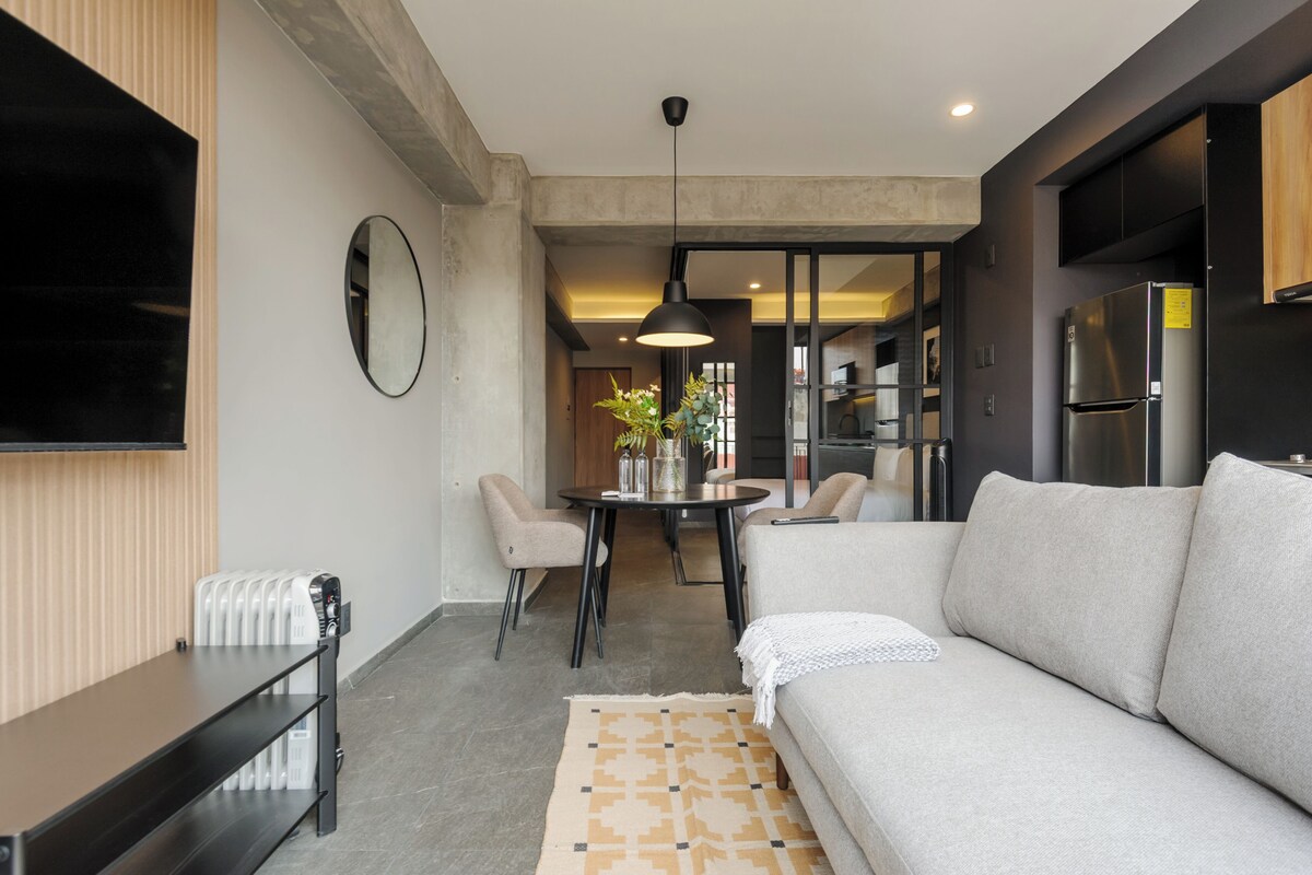 A modern living room with a sofa, a coffee table, a TV, and a dining area with chairs and a table.