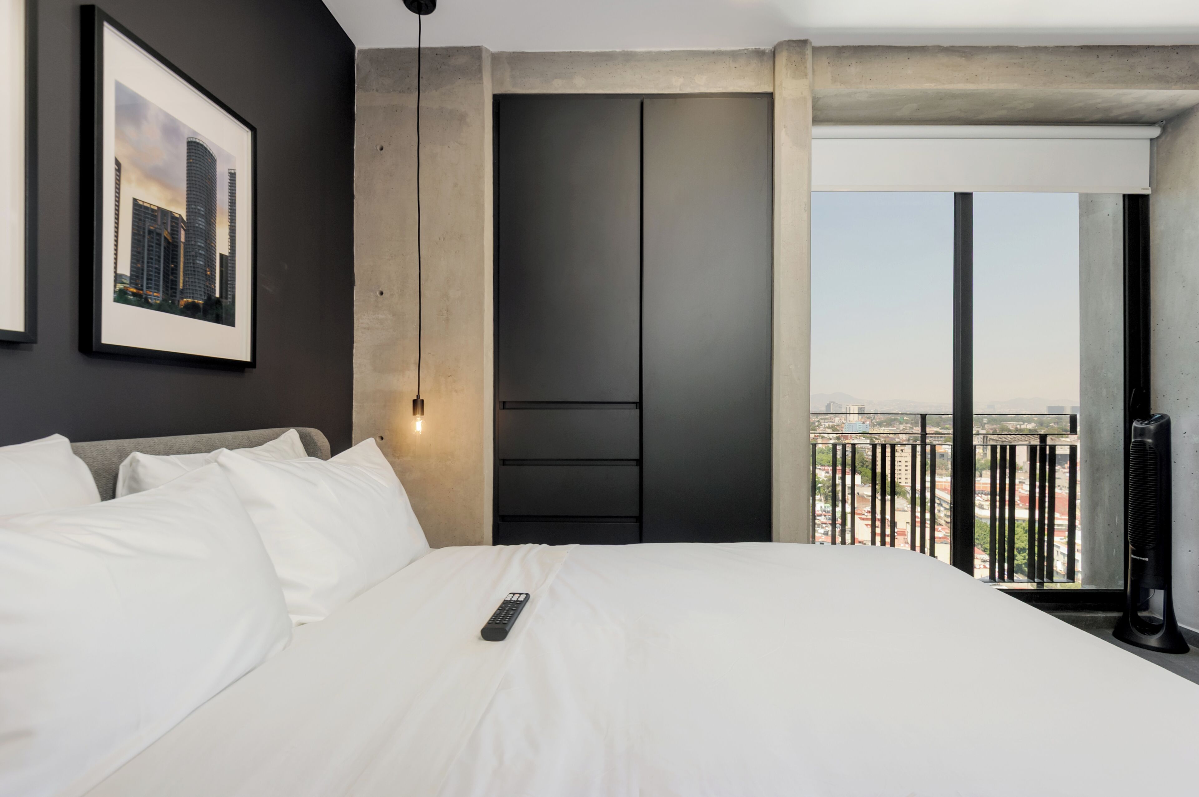 Une chambre d’hôtel avec un lit, un tableau encadré au mur, une armoire et un balcon donnant sur la ville.