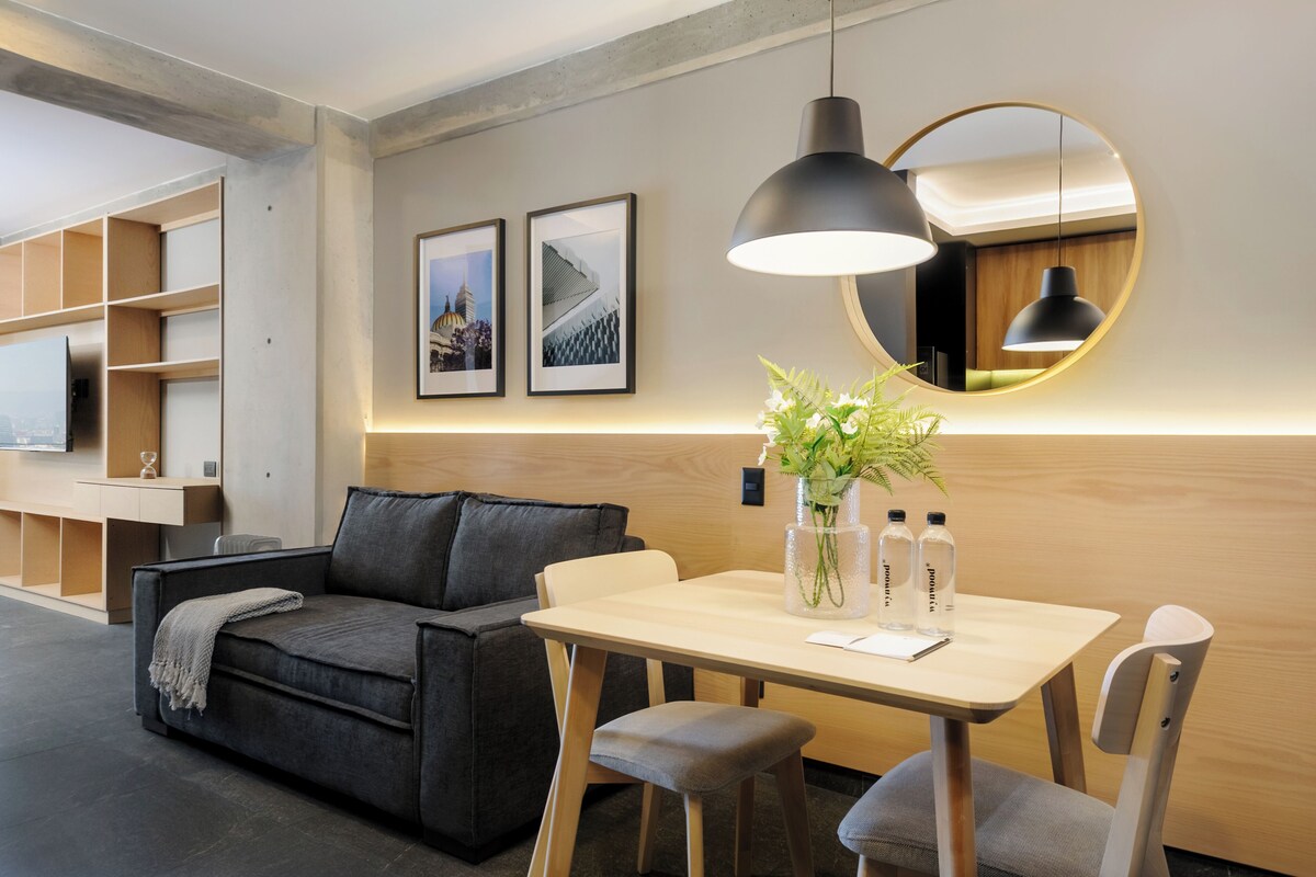 A modern room with a sofa, a table with a vase of flowers, and a mirror with a round frame.