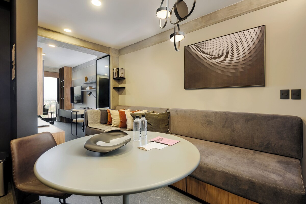 A modern living room with a round table, a sofa, and a large abstract painting on the wall.