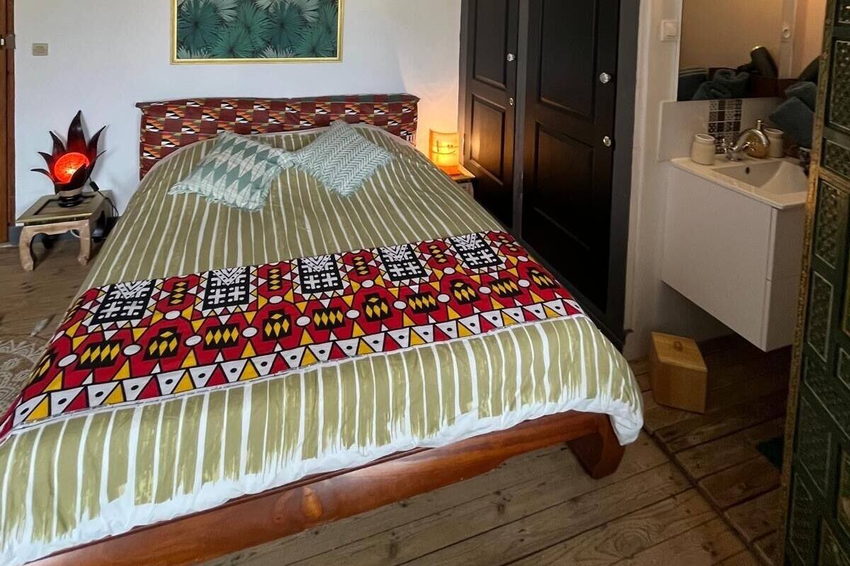 A bedroom with a bed, a hanging light fixture, a wall-mounted mirror, and a door with a decorative panel.