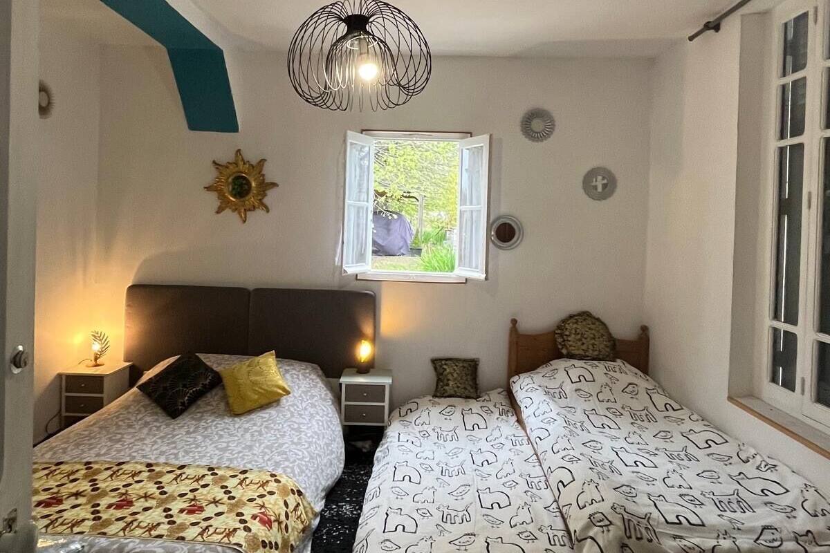 A bedroom with two beds, a window with a view, a hanging light fixture, and a small table with a lamp.